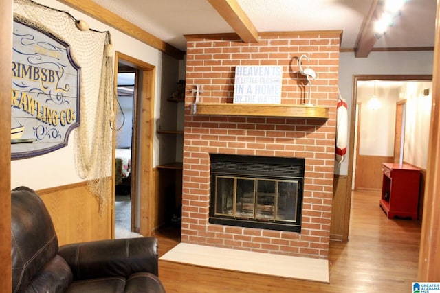 living area featuring beam ceiling, wainscoting, wood finished floors, and a fireplace
