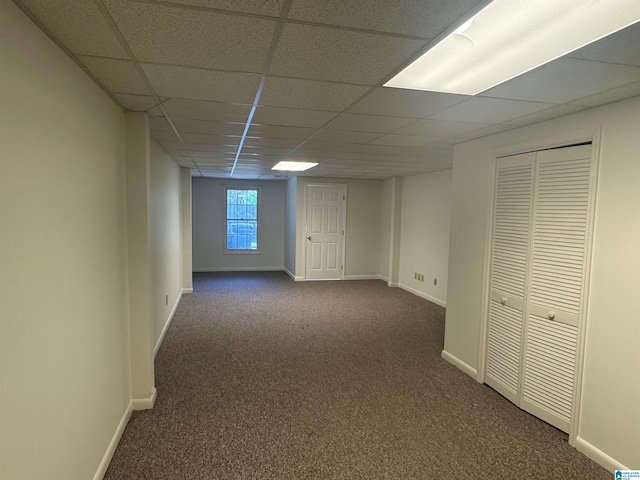 below grade area featuring dark carpet, a drop ceiling, and baseboards