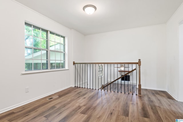 empty room featuring baseboards, visible vents, ornamental molding, and wood finished floors