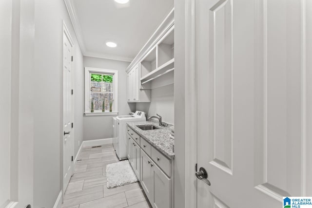 washroom featuring a sink, cabinet space, washing machine and clothes dryer, baseboards, and ornamental molding