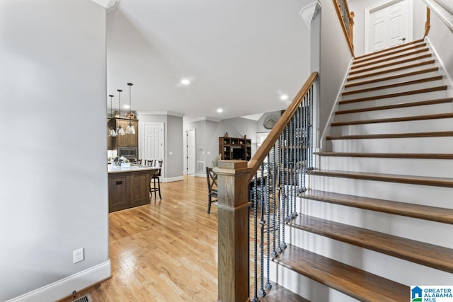 staircase with baseboards, recessed lighting, ornamental molding, a fireplace, and wood finished floors