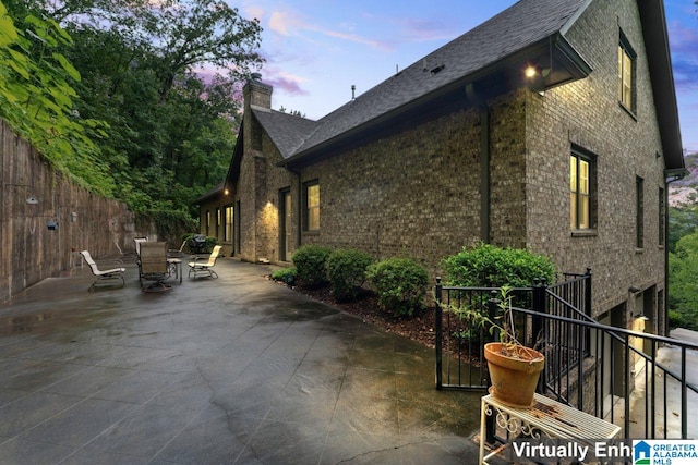 property exterior at dusk with outdoor dining space, a chimney, a patio area, and brick siding