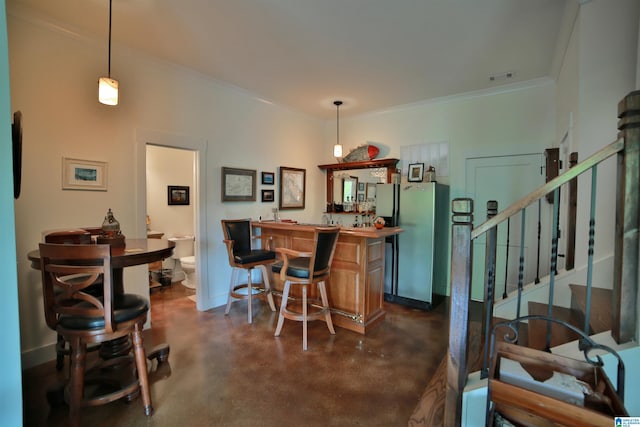bar with finished concrete flooring, indoor wet bar, ornamental molding, and freestanding refrigerator