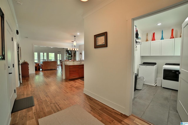 hallway featuring a sink, light wood-style floors, baseboards, separate washer and dryer, and recessed lighting