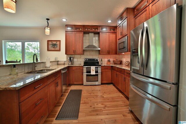 kitchen with brown cabinets, a sink, appliances with stainless steel finishes, wall chimney exhaust hood, and a peninsula