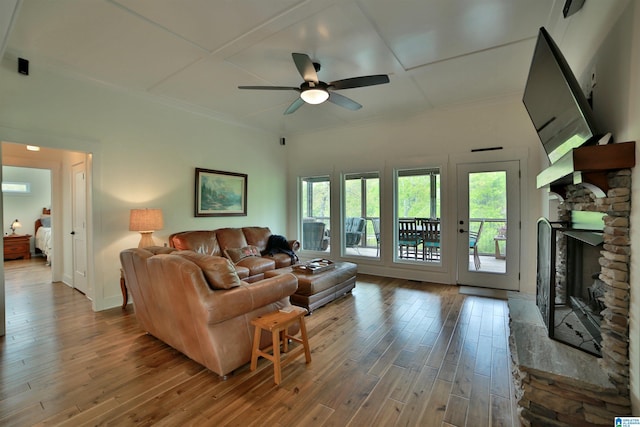 living room featuring wood-type flooring, ceiling fan, a stone fireplace, and ornamental molding