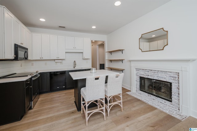 kitchen featuring light countertops, dark cabinetry, a sink, black appliances, and a kitchen bar