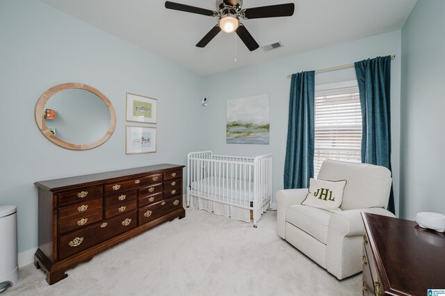 bedroom featuring a nursery area, visible vents, light colored carpet, and ceiling fan