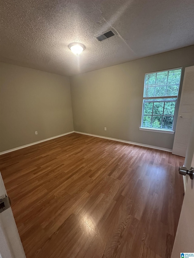 spare room featuring baseboards, wood finished floors, visible vents, and a textured ceiling
