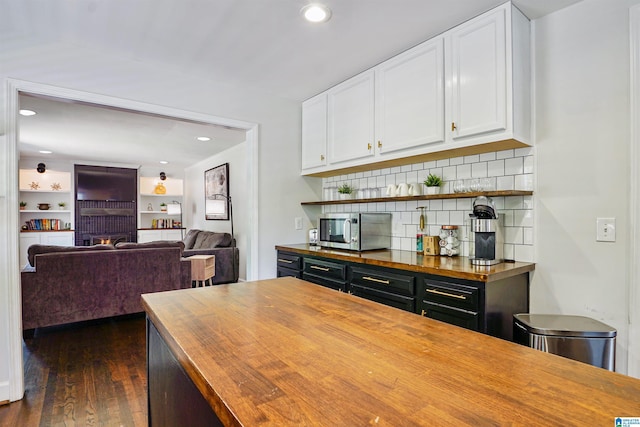 interior space featuring decorative backsplash, white cabinets, stainless steel microwave, dark wood-style floors, and butcher block countertops