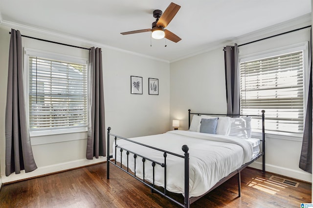 bedroom featuring a ceiling fan, baseboards, wood finished floors, visible vents, and ornamental molding