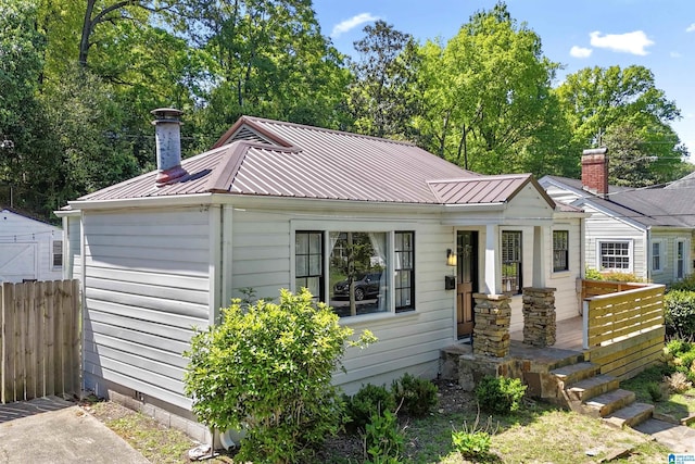 bungalow-style home with fence, metal roof, and a chimney
