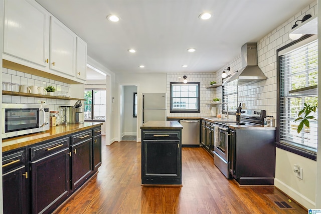 kitchen with stainless steel appliances, open shelves, wall chimney exhaust hood, and tasteful backsplash