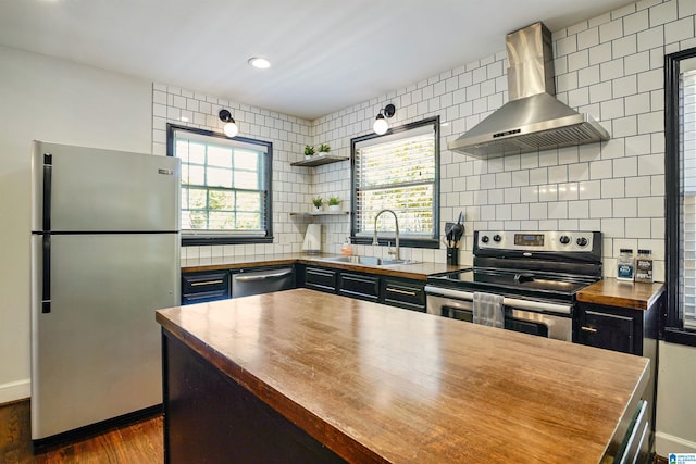 kitchen featuring dark wood-style flooring, wall chimney exhaust hood, a sink, wood counters, and appliances with stainless steel finishes