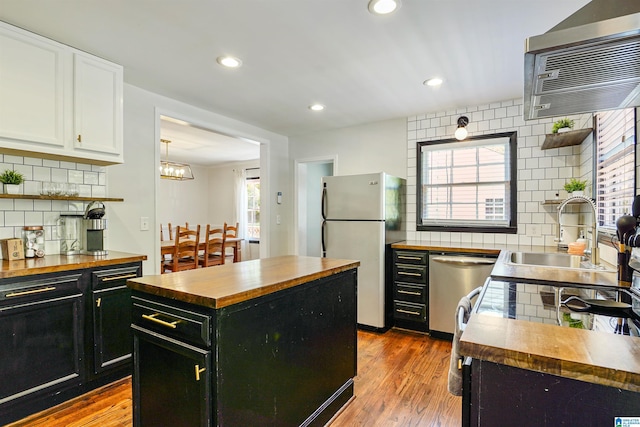 kitchen featuring appliances with stainless steel finishes, a sink, dark cabinets, wooden counters, and backsplash