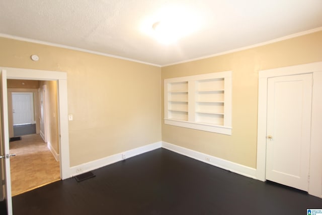 empty room with built in shelves, dark wood-type flooring, crown molding, and baseboards