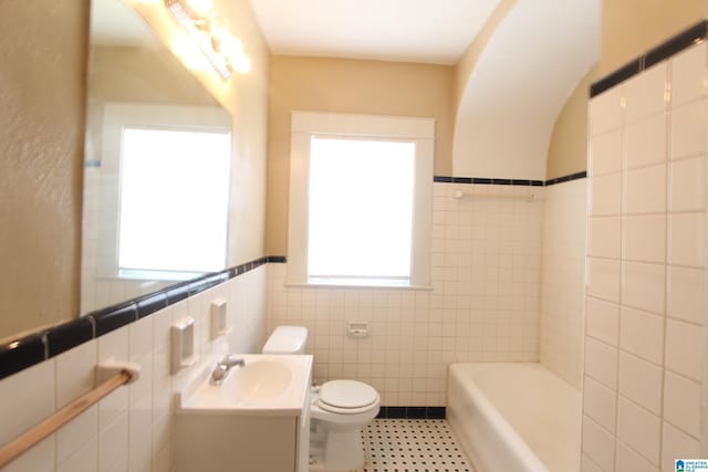 full bathroom featuring toilet, vanity, tile walls, wainscoting, and a bathtub