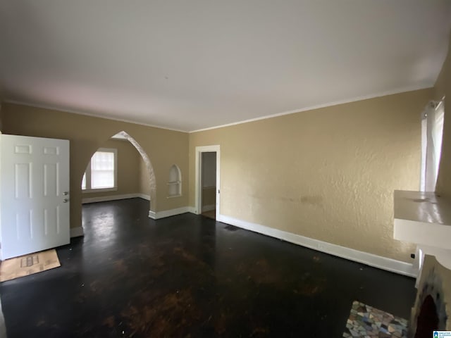 unfurnished living room featuring arched walkways, crown molding, and baseboards
