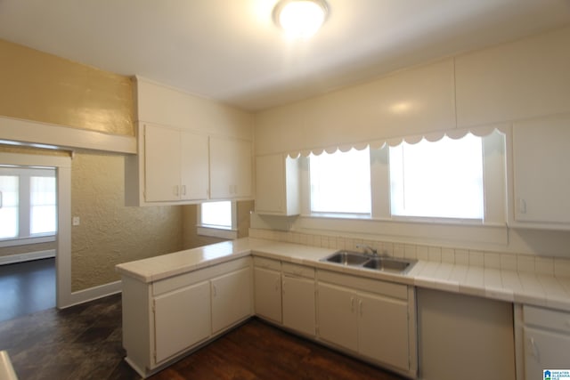 kitchen with white cabinets, a textured wall, tile countertops, a sink, and a peninsula