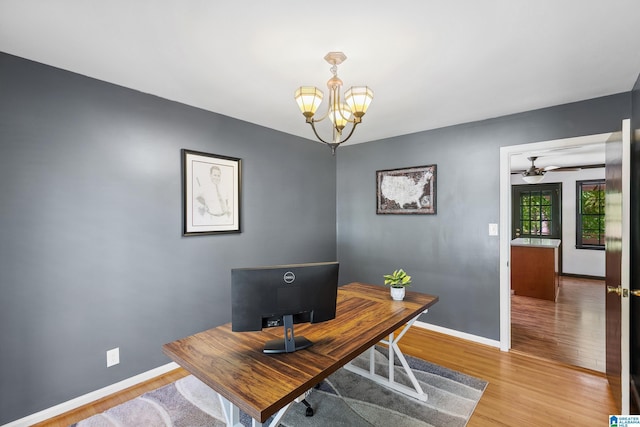 office featuring light wood-type flooring, baseboards, and ceiling fan with notable chandelier