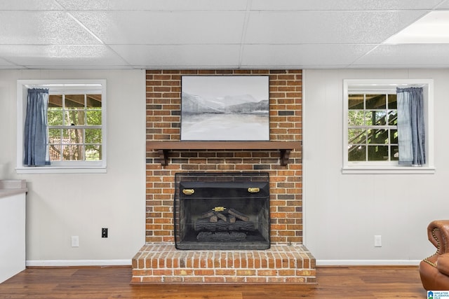 living room with a fireplace, wood finished floors, a drop ceiling, and baseboards