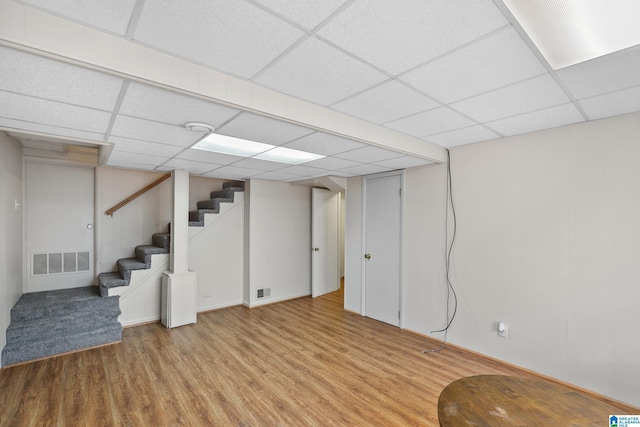 finished basement with stairway, a drop ceiling, wood finished floors, and visible vents