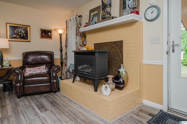 living area featuring a brick fireplace, visible vents, and wood finished floors