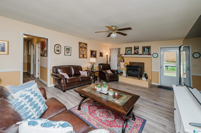 living room with a textured ceiling, a fireplace with raised hearth, baseboards, wood finished floors, and a ceiling fan