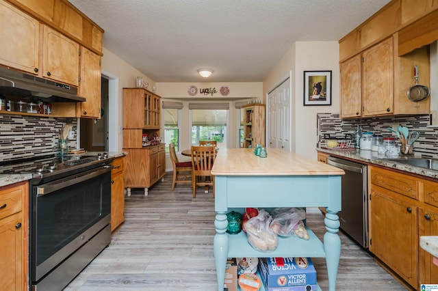 kitchen with tasteful backsplash, appliances with stainless steel finishes, under cabinet range hood, and light wood-style floors