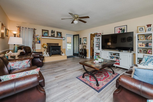 living room with a fireplace with raised hearth, a ceiling fan, baseboards, a textured ceiling, and wood finished floors