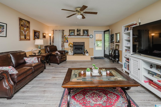 living area with wood finished floors, a fireplace with raised hearth, and a ceiling fan