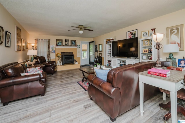 living room featuring wood finished floors, ceiling fan, a textured ceiling, and a fireplace with raised hearth