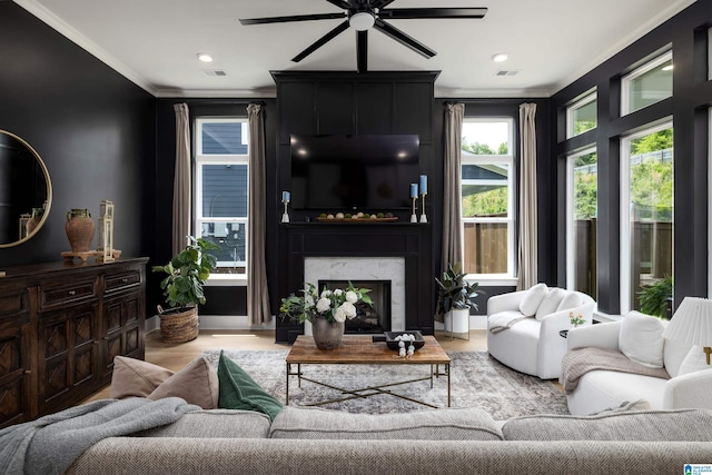 living room featuring light wood-style floors, ornamental molding, ceiling fan, a fireplace, and visible vents