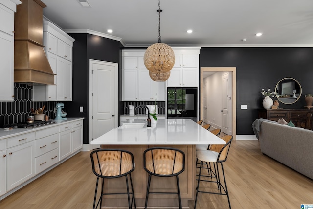 kitchen featuring decorative backsplash, a chandelier, a breakfast bar, a sink, and premium range hood