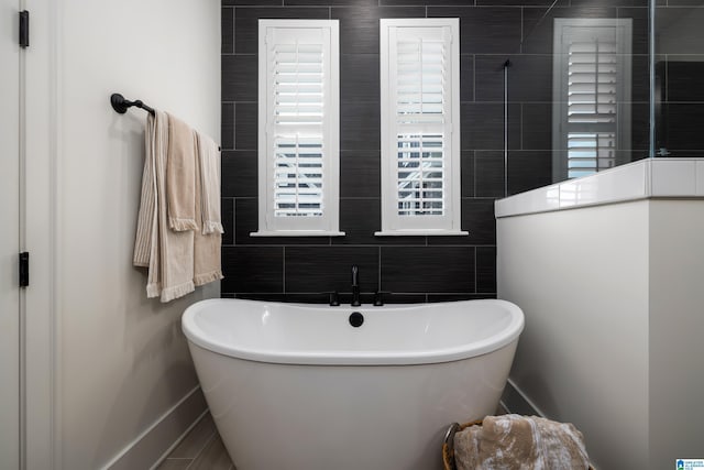 full bathroom with a walk in shower, a soaking tub, baseboards, and tile walls