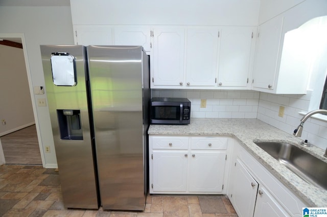 kitchen with a sink, appliances with stainless steel finishes, white cabinets, and stone finish floor