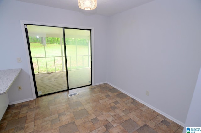 unfurnished room featuring baseboards, stone finish flooring, and visible vents