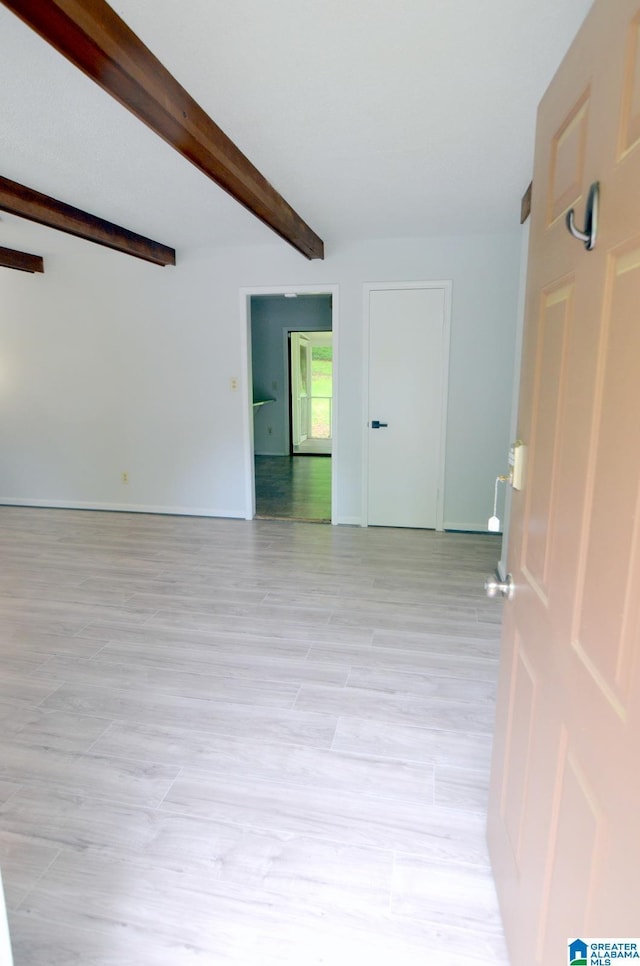 empty room with baseboards, light wood-type flooring, and beam ceiling