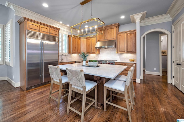 kitchen featuring a sink, built in fridge, baseboards, arched walkways, and under cabinet range hood