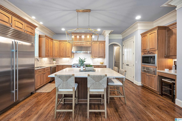 kitchen with a sink, built in appliances, a warming drawer, a center island, and arched walkways