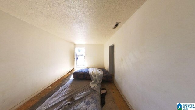 bedroom featuring wood finished floors, a textured ceiling, baseboards, and visible vents