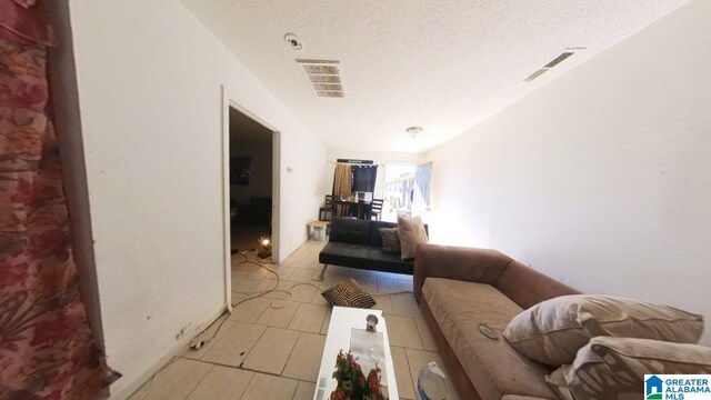 hallway with visible vents, a textured ceiling, and light tile patterned floors