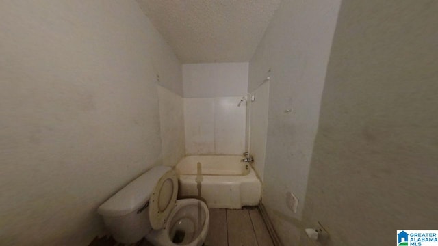 full bath with toilet, washtub / shower combination, and a textured ceiling