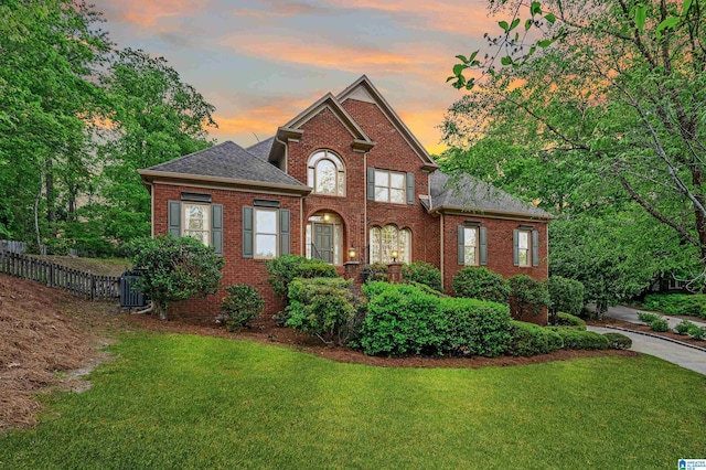 view of front of property with brick siding, a yard, central AC, roof with shingles, and fence