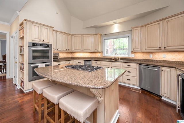 kitchen with tasteful backsplash, cream cabinets, stainless steel appliances, a kitchen island, and a sink