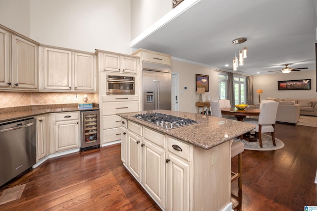 kitchen with beverage cooler, stainless steel appliances, ornamental molding, open floor plan, and cream cabinetry