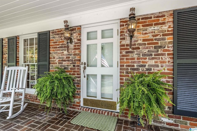 doorway to property with a porch and brick siding