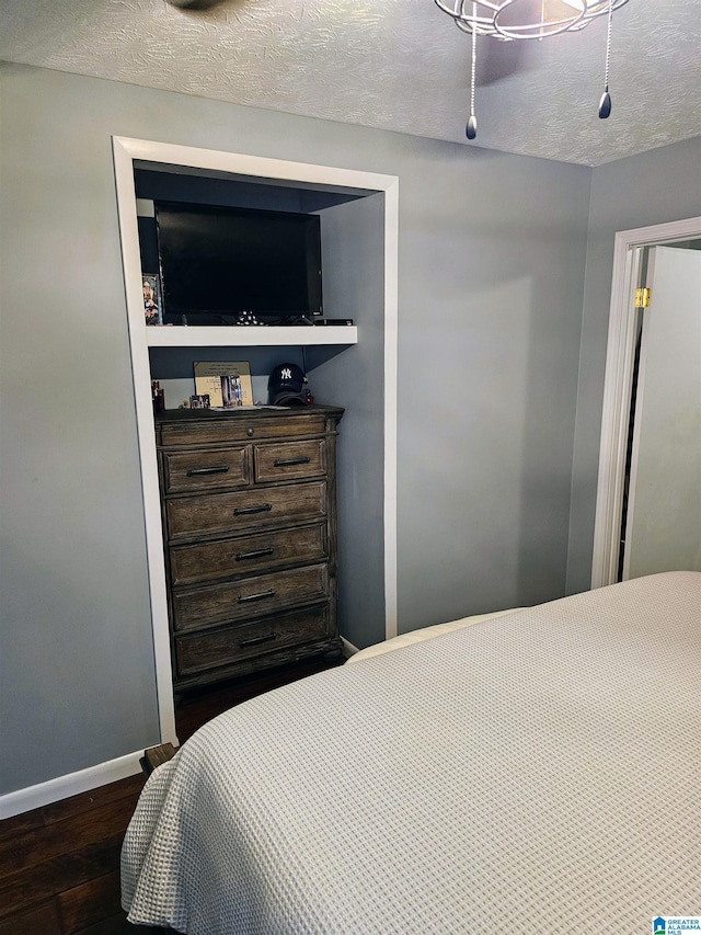 bedroom featuring baseboards, wood finished floors, a textured ceiling, and ceiling fan