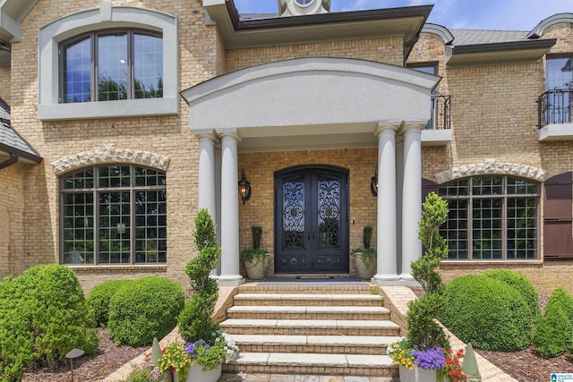 property entrance featuring french doors, brick siding, covered porch, and a balcony