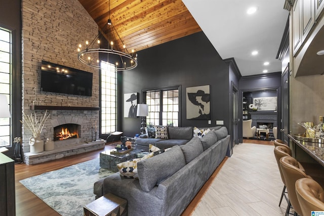 living room with a chandelier, wood ceiling, a stone fireplace, high vaulted ceiling, and ornamental molding